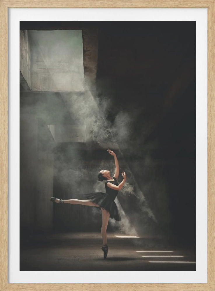 A ballerina in a black tutu gracefully performs an arabesque in a vast, dark, industrial space filled with smoke, dramatically illuminated by shafts of light from above. Poster