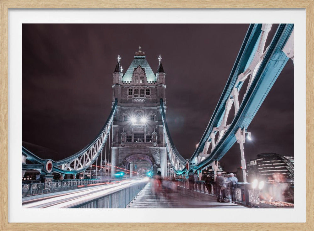 A framed, long-exposure night photograph of London's Tower Bridge taken from the pedestrian walkway. The iconic bridge tower and its blue suspension structure are brightly lit against a dark, cloudy sky, with streaks of white and red light from traffic blurring along the roadway. Print