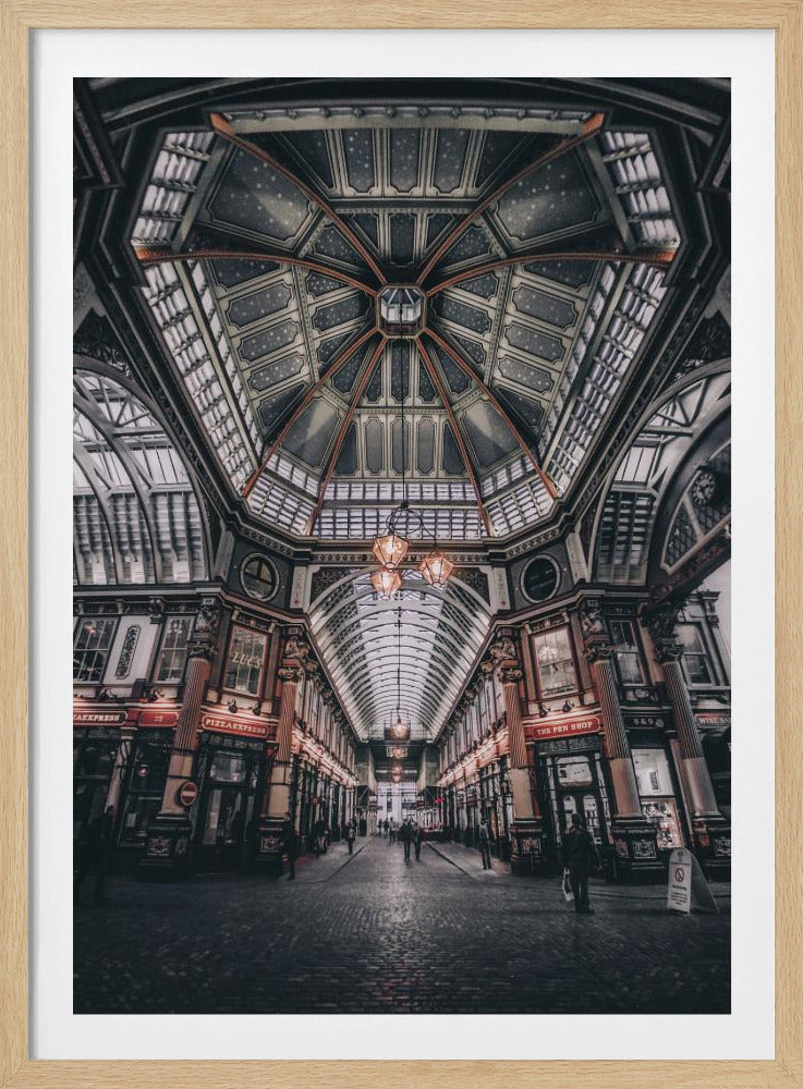 A wide-angle, symmetrical photograph looking down the center of an ornate Victorian covered market, Leadenhall Market. The focus is on the elaborate, arched glass and ironwork ceiling which is decorated in dark blue with gold stars. Below, a cobblestone path is lined with traditional shops with glowing lights, and a few people can be seen walking in the distance. The image has a moody, high-contrast aesthetic. Wall Art
