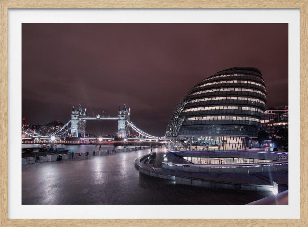 A framed nighttime photograph of London's cityscape, featuring the illuminated, modern, curved architecture of City Hall on the right and the iconic Tower Bridge glowing in the background over the River Thames, under a dark purple sky. Artwork