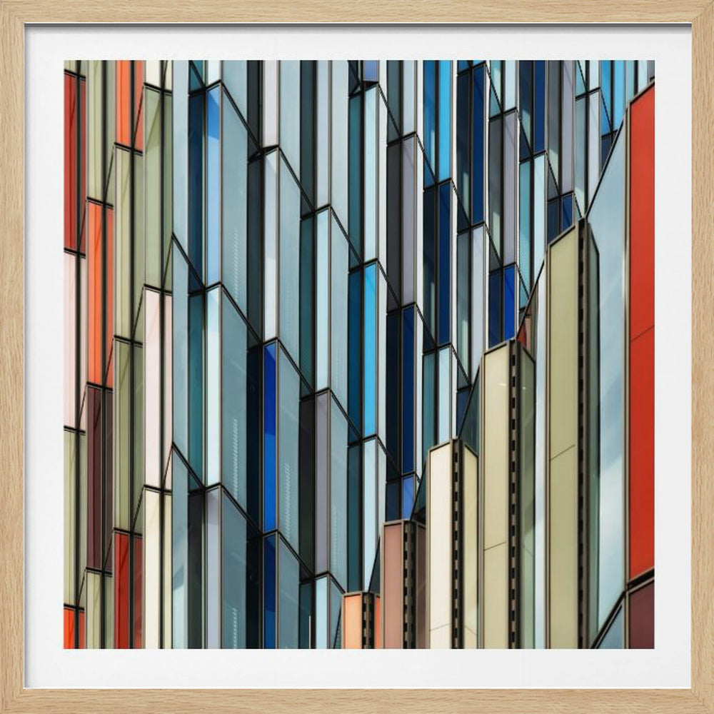 A close-up abstract photograph of a modern building's facade, featuring a complex pattern of colorful, angular glass panels in shades of blue, orange, red, and gray, all presented within a light wood frame. Wall Art