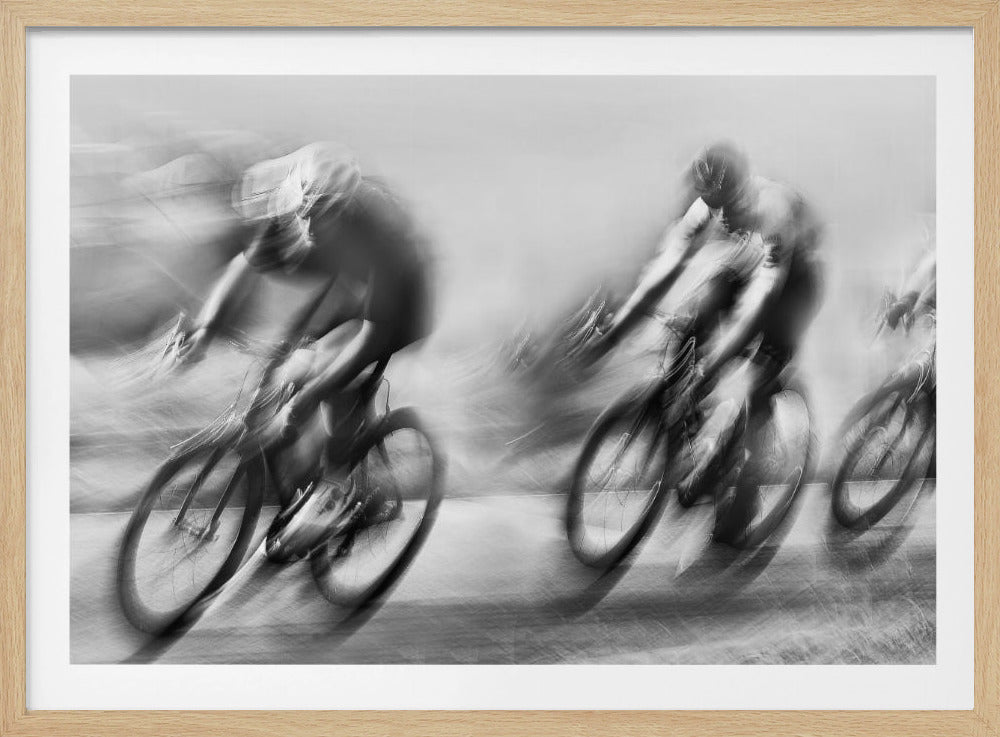 A dynamic black and white action photograph of three cyclists racing, captured with a slow shutter speed to create a dramatic motion blur effect. The riders and their bikes are blurred into streaks of light and shadow, conveying a powerful sense of speed and intensity. The image is presented within a silver-toned frame. Poster