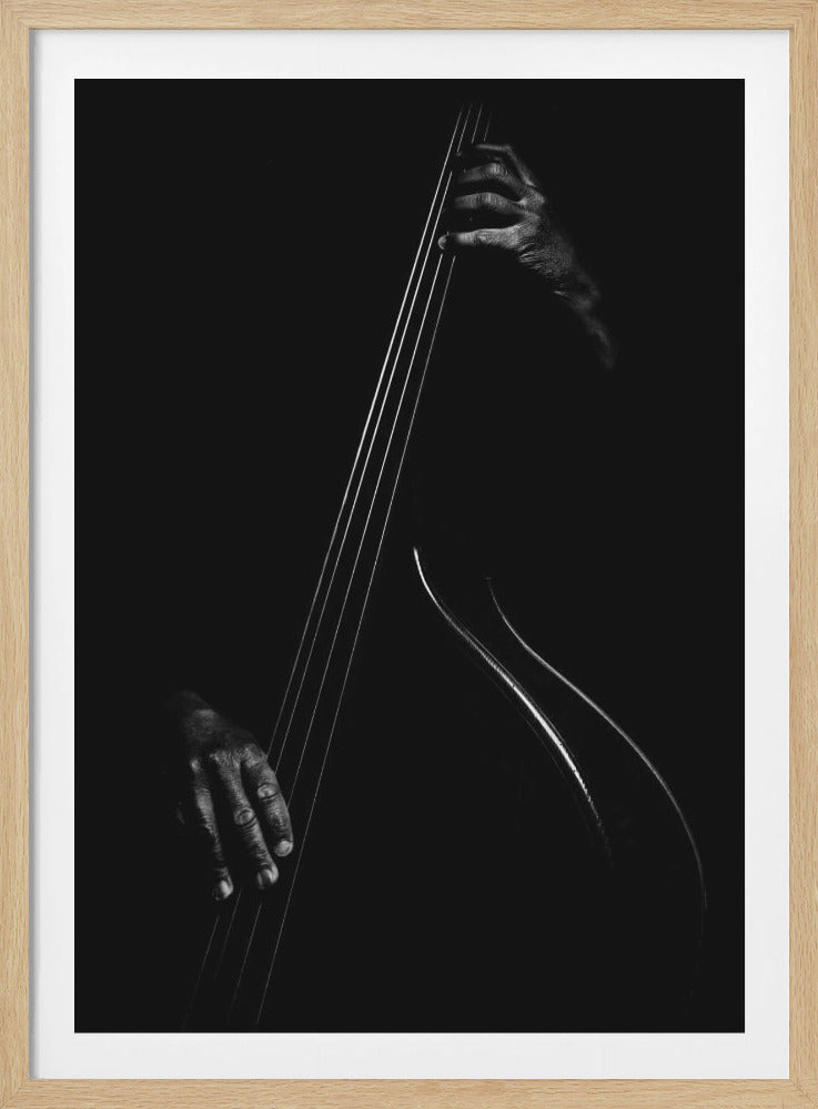 A dramatic black and white close-up photograph of a musician's hands playing an upright bass. The image is set against a pure black background, with stark lighting highlighting the strings, the curve of the instrument's body, and the texture of the musician's hands. Print