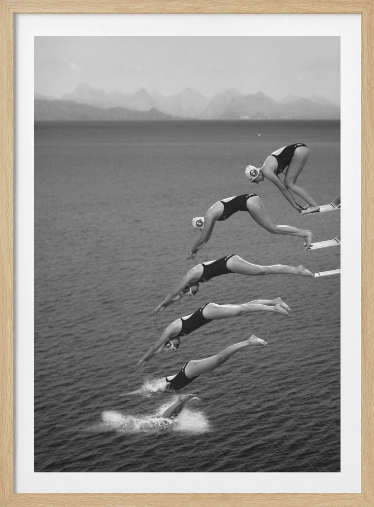 A black and white composite photograph capturing the sequential motion of a female swimmer diving off a board into the ocean. The image shows multiple stages of her dive, from crouching on the board to entering the water, creating a graceful arc against the backdrop of the sea and distant mountains. Print