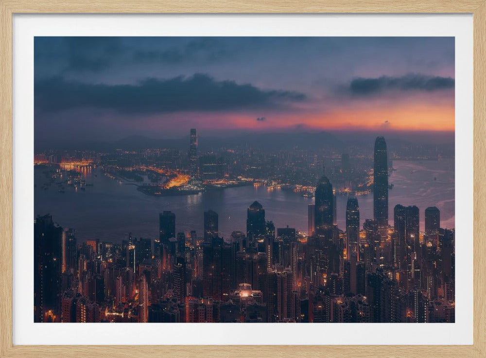 An aerial photograph of a sprawling city skyline at dusk, likely Hong Kong, with countless illuminated skyscrapers. The sky above transitions from a warm orange glow at the horizon to a deep purple, with dark clouds overhead. The city lights cast a golden reflection on the water of the harbor. The entire image is presented within a silver-colored frame. Poster