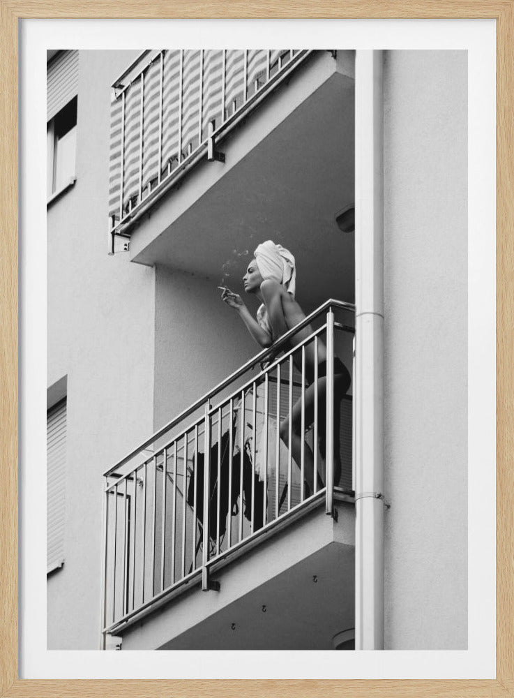 A black and white photo of a woman with a towel on her head, smoking a cigarette on an apartment balcony. The low-angle shot captures her leaning on the metal railing, with smoke drifting from the cigarette. Print