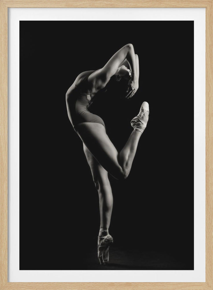 A dramatic black and white studio photograph of a ballerina balancing on one pointe shoe. She is in a deep backbend, with one leg lifted high, her form and musculature highlighted by stark lighting against a pure black background. Print