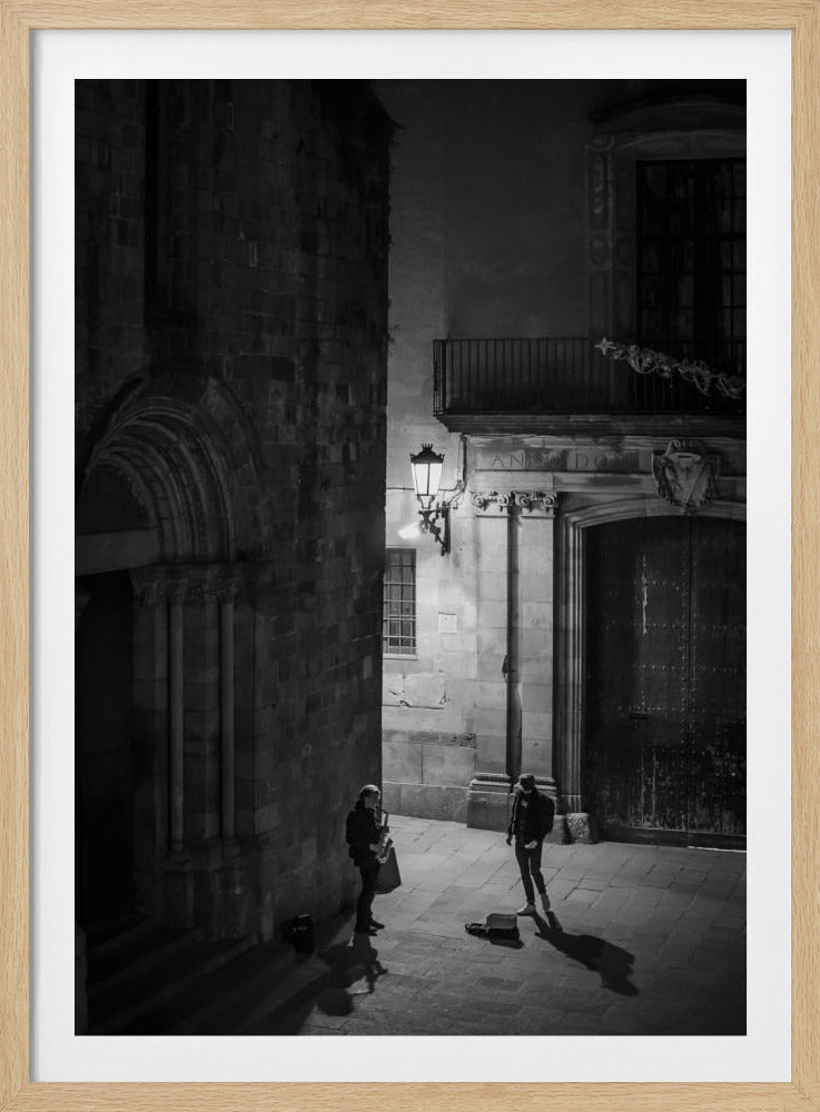 A high-angle, black and white photograph of a street musician playing a saxophone for a lone listener in a narrow stone alley at night. The scene is illuminated by an ornate streetlamp, casting long shadows on the cobblestone ground. Wall Art