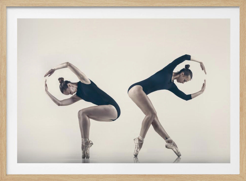 A framed photograph showing two poses of a female ballet dancer in a black leotard and pointe shoes against a stark white background, her arms gracefully curved above her head. Poster