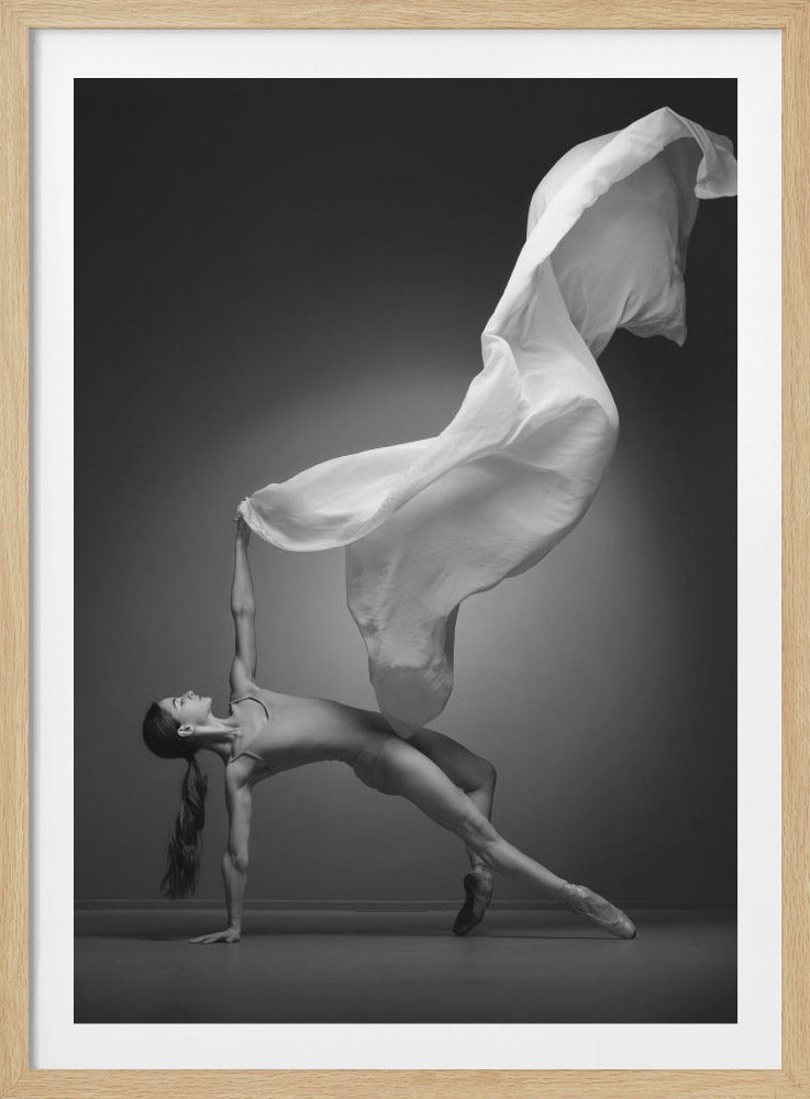 A black and white studio photograph of a graceful ballerina in a dynamic pose, leaning back with one hand on the floor while her other hand raises a large, flowing piece of white fabric above her head against a grey background. Artwork