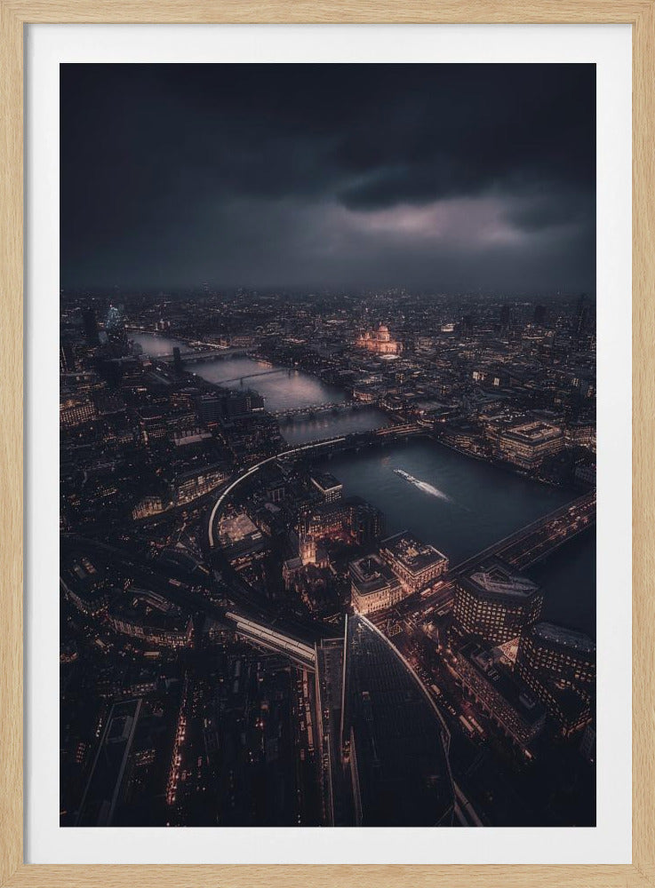 An aerial photograph of London at night from a high vantage point, overlooking the winding River Thames illuminated by the golden glow of city lights under a dark, dramatic, and cloudy sky. Wall Art