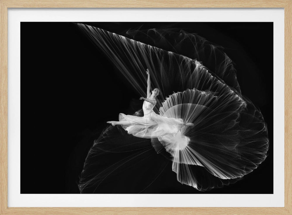 A dynamic black and white photograph of a ballerina in a white dress, frozen mid-leap in a split position. A stroboscopic light effect creates a sweeping, ethereal fan of light that trails behind her, capturing the full arc of her movement against a stark black background. The image is enclosed in a silver frame. Print