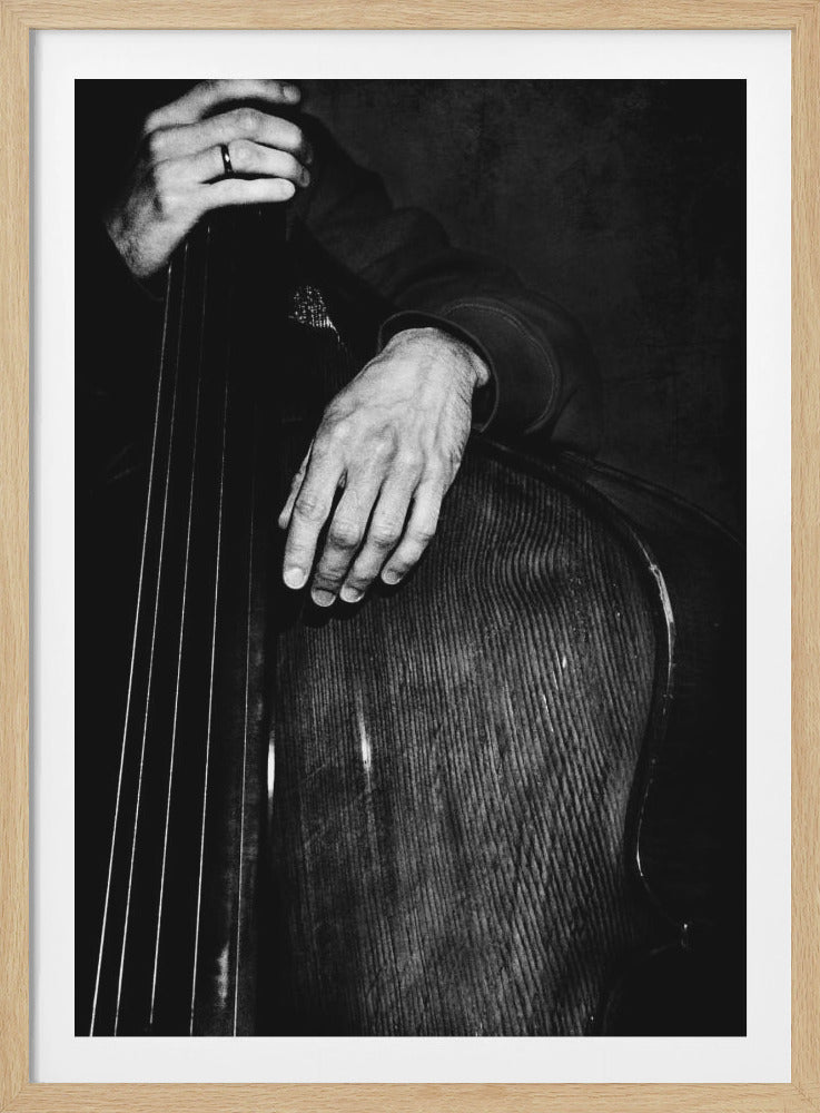 A moody black and white close-up photograph of a musician's hands resting on the neck and body of a wooden double bass. One hand, wearing a dark ring, is positioned high on the neck, while the other rests on the curved body of the instrument. Decor