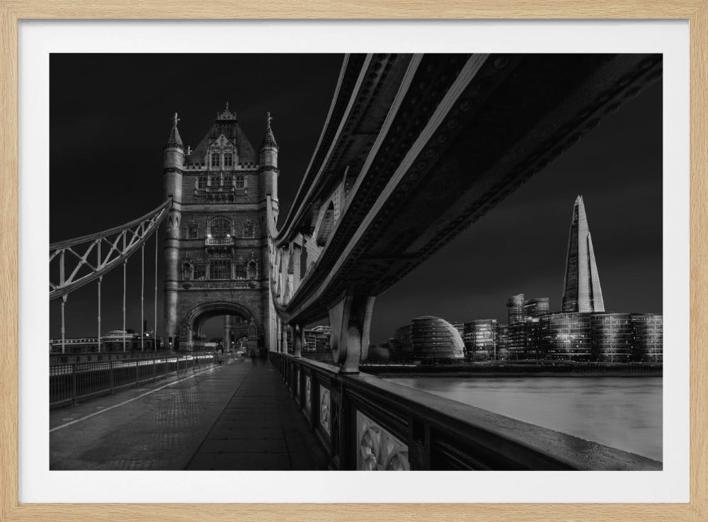 A dramatic, low-angle black and white photograph of London's Tower Bridge at night, taken from the pedestrian walkway. The image showcases the architectural details of the bridge and the illuminated modern city skyline, including The Shard, across the River Thames. Print