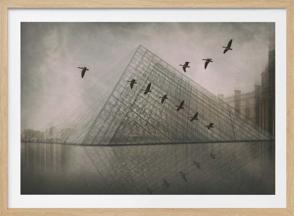 A moody, artistic photograph of a flock of geese flying in a diagonal formation in front of the glass Louvre Pyramid. The scene is foggy and has a desaturated, almost monochromatic color palette, with the pyramid and birds reflected in the water below. The image is displayed in a silver frame. Poster