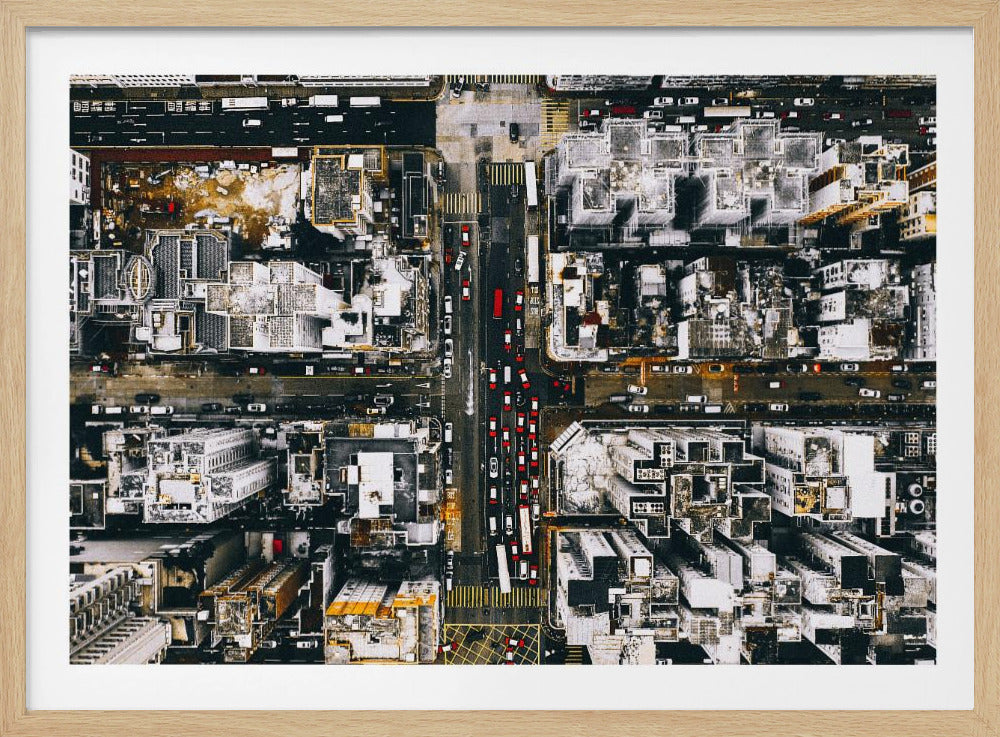 A framed, top-down aerial photo of a dense city grid. The monochromatic scene of white rooftops and dark streets is punctuated by the red and white cars creating lines of traffic below. Decor