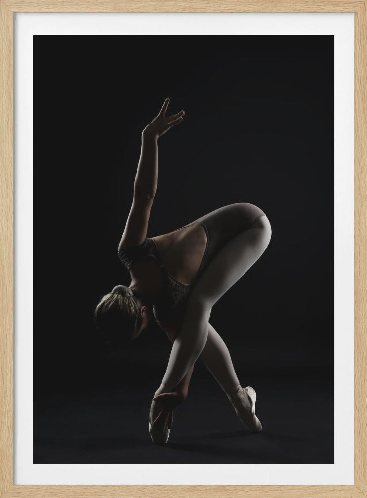A dramatic studio photograph of a ballerina in a complex pose against a solid black background. Strong rim lighting highlights the graceful curves of her body as she bends forward with her legs crossed, one arm extended high and the other reaching towards her pointe shoes. Poster