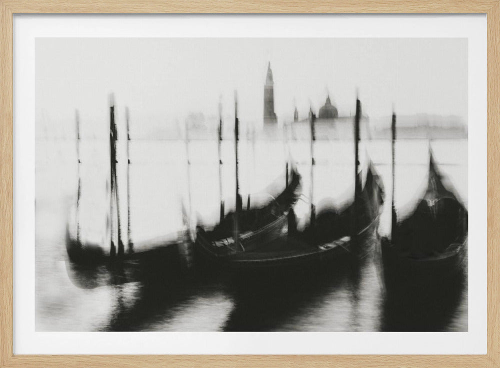An abstract, black and white photograph with a motion blur effect depicting gondolas moored in Venice. The dark silhouettes of the boats are in the foreground, with the faint, hazy outlines of Venetian architecture, including a bell tower and dome, visible in the background against a light grey sky. The image is presented in a silver frame. Poster