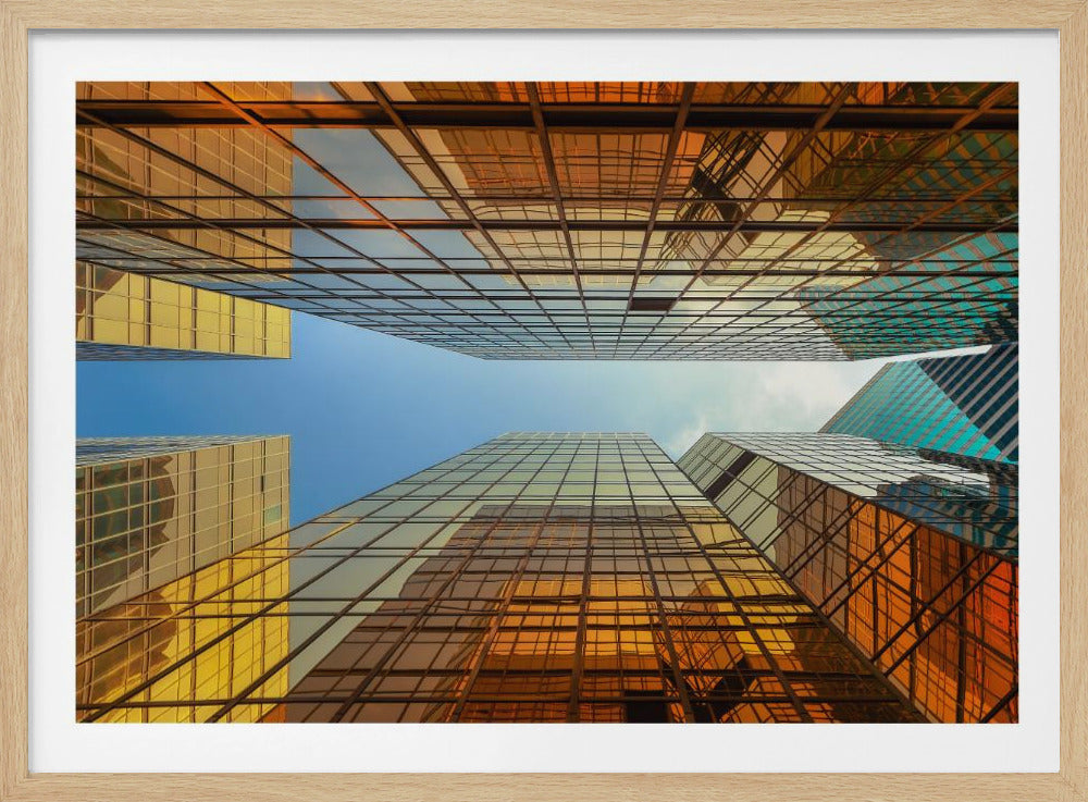 A low-angle, upward view of modern skyscrapers with golden reflective glass windows, creating a geometric pattern against a narrow strip of clear blue sky. Decor
