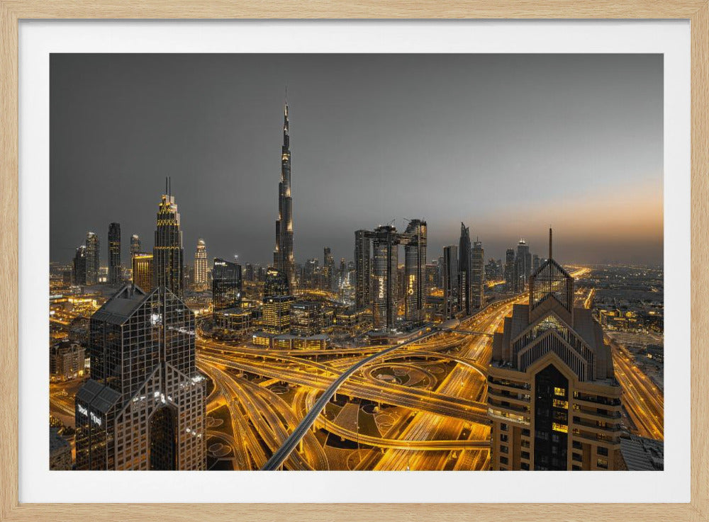 A framed, high-angle, long-exposure photograph of the Dubai skyline at dusk. The towering Burj Khalifa stands out against a grey sky, while the city's skyscrapers are illuminated. In the foreground, a complex network of highways glows with the yellow light trails of traffic, creating intricate patterns. Poster