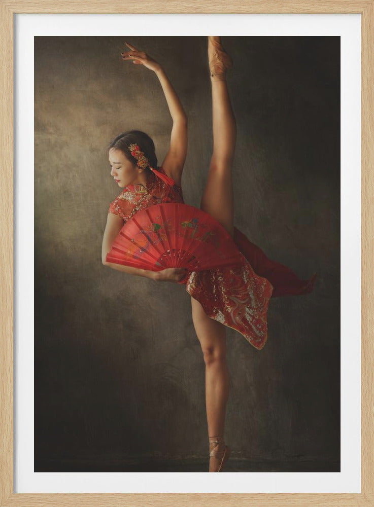 An elegant ballet dancer in a red, ornate Chinese dress performs a standing split while holding a matching red fan against a dark, textured gray background. Decor