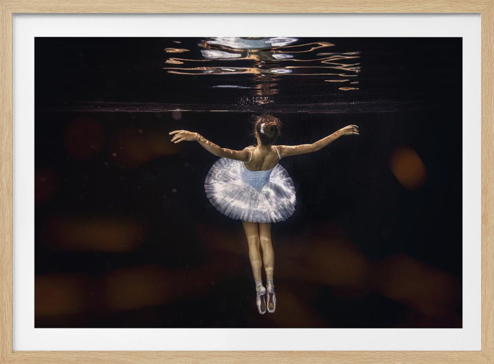 A ballerina seen from behind, wearing a white tutu and pointe shoes, gracefully suspended underwater in a classic ballet pose against a dark background with her reflection on the water's surface. Decor
