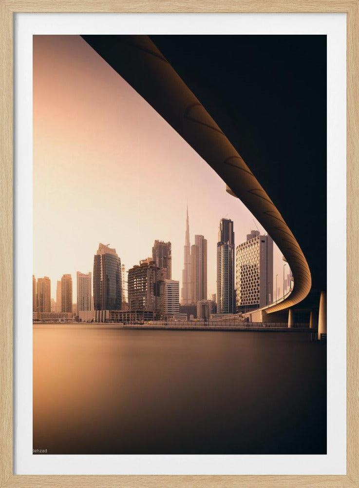 A view of the Dubai skyline, including the Burj Khalifa, framed by the sweeping curve of a bridge in the foreground. The city is bathed in the warm, soft light of a sunrise or sunset, with its reflection visible on the calm water below. Decor