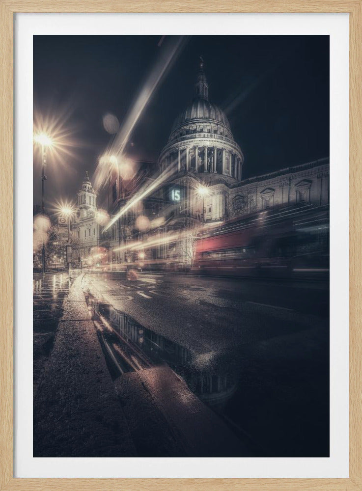 A dynamic long-exposure photograph of a wet London street at night, with the iconic dome of St. Paul's Cathedral illuminated in the background. Streaks of light from passing traffic, including a red bus, blur across the scene, while the glistening pavement reflects the cathedral and bright streetlights. Decor