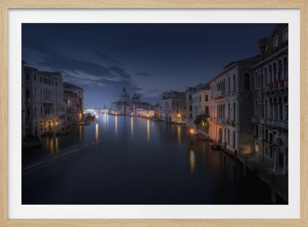 A serene night photograph of the Grand Canal in Venice, Italy. Historic buildings with warm, glowing lights line the calm, dark water, with their reflections shimmering on the surface. In the distance, the iconic dome of the Basilica di Santa Maria della Salute is silhouetted against a deep blue twilight sky. Decor
