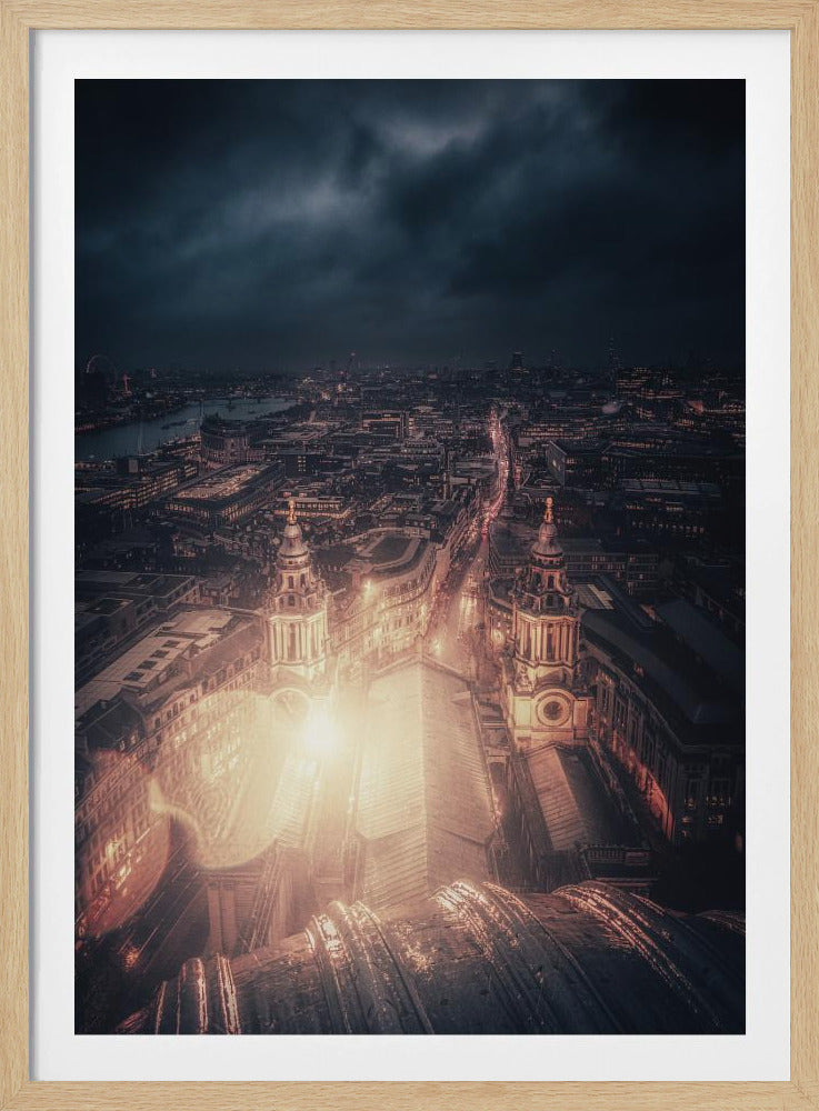 A dramatic, high-angle nighttime photograph of a sprawling city, likely London, viewed from the top of a cathedral. The foreground shows the curved dome, while below, two towers and the long roof of the church are brightly illuminated. The city stretches into the distance with countless golden lights under a dark, stormy, and cloud-filled sky. Poster