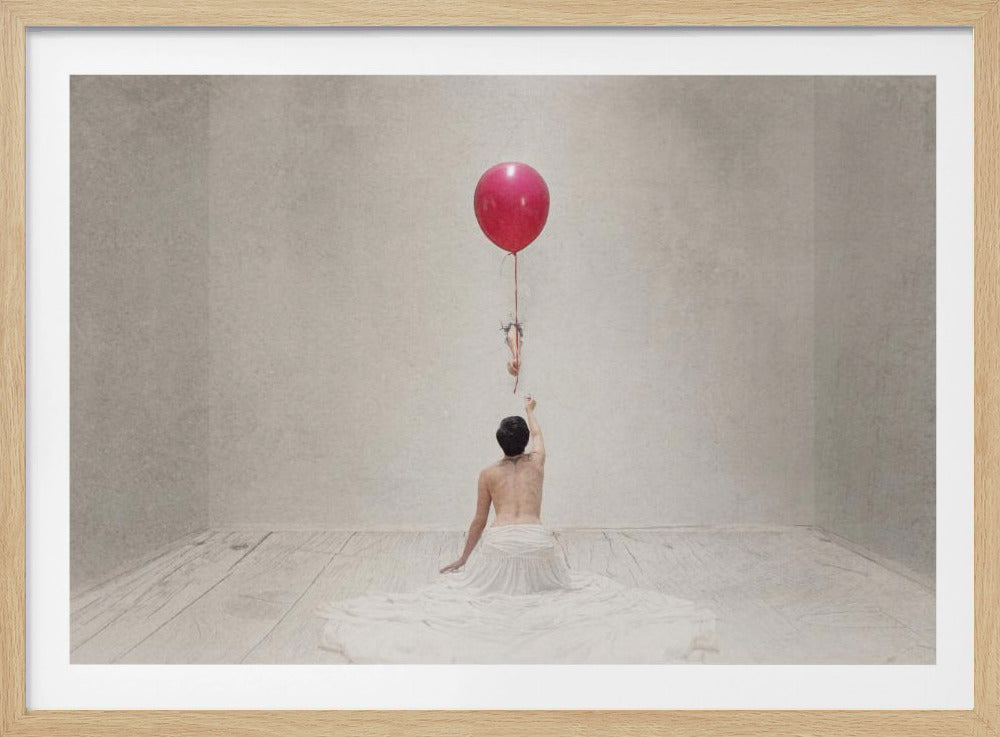 A surreal fine art photograph of a person with a bare back and a long white skirt, sitting on the floor of a minimalist grey room. They are reaching up towards a small figure hanging from the string of a large, bright red balloon that floats towards the ceiling. The image is enclosed in a silver frame. Artwork