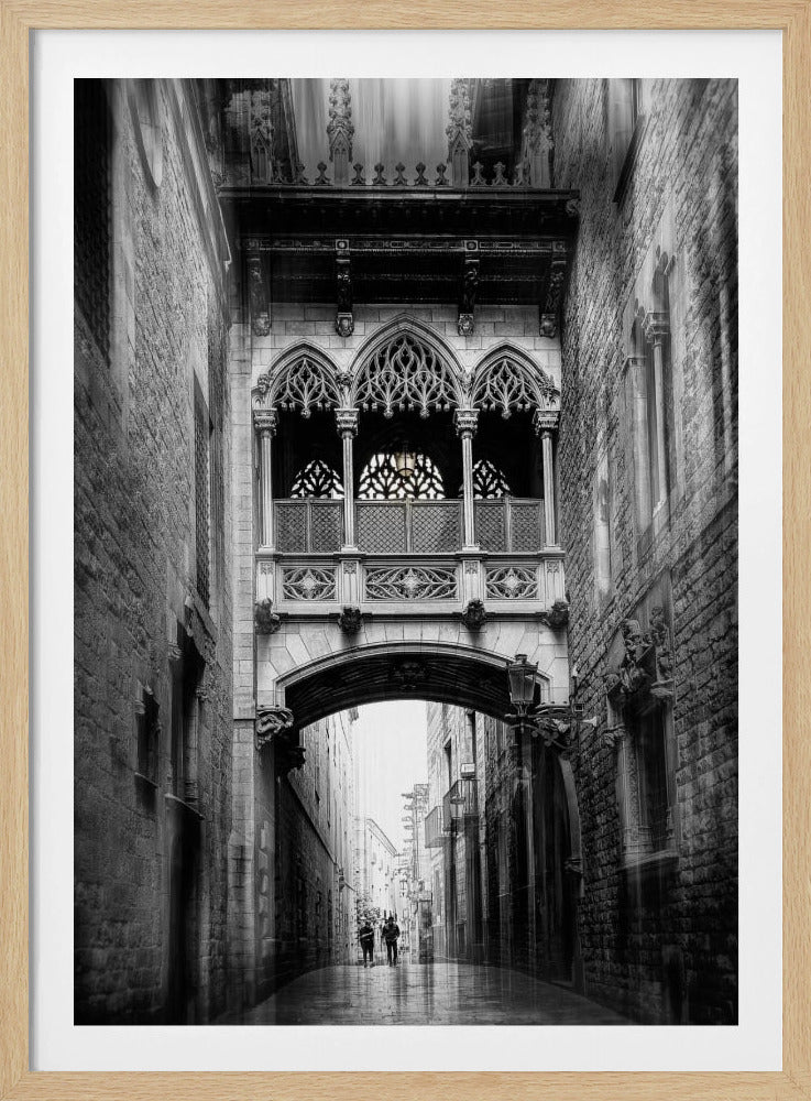 A moody, vertical black and white photograph of an ornate Gothic-style bridge connecting two stone buildings over a narrow alleyway. Below the arch of the bridge, the wet street stretches into the distance where two figures are walking away. Decor