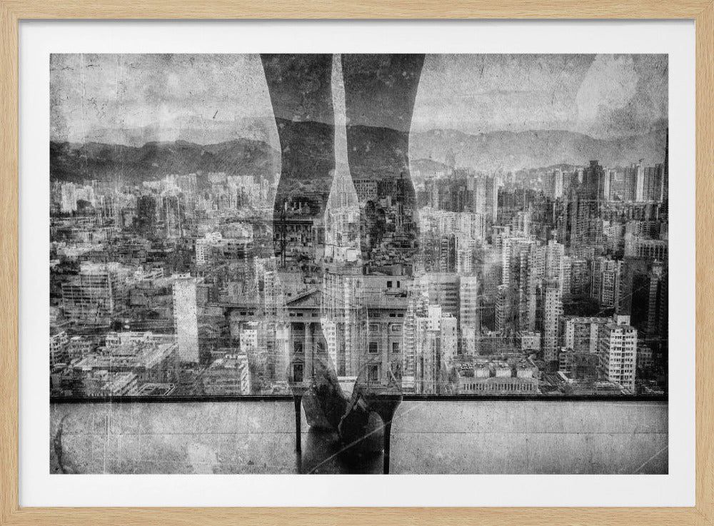 A framed, black and white artistic photograph featuring a double exposure. A vast, dense cityscape with distant mountains is visible through the translucent silhouette of a person's legs standing on a balcony edge. Poster