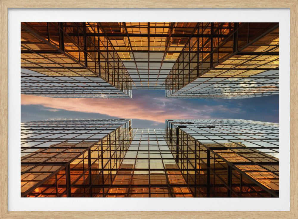 A framed photograph showing a worm's-eye view looking up at a sunset sky between four modern skyscrapers with golden-tinted, reflective glass facades. Print