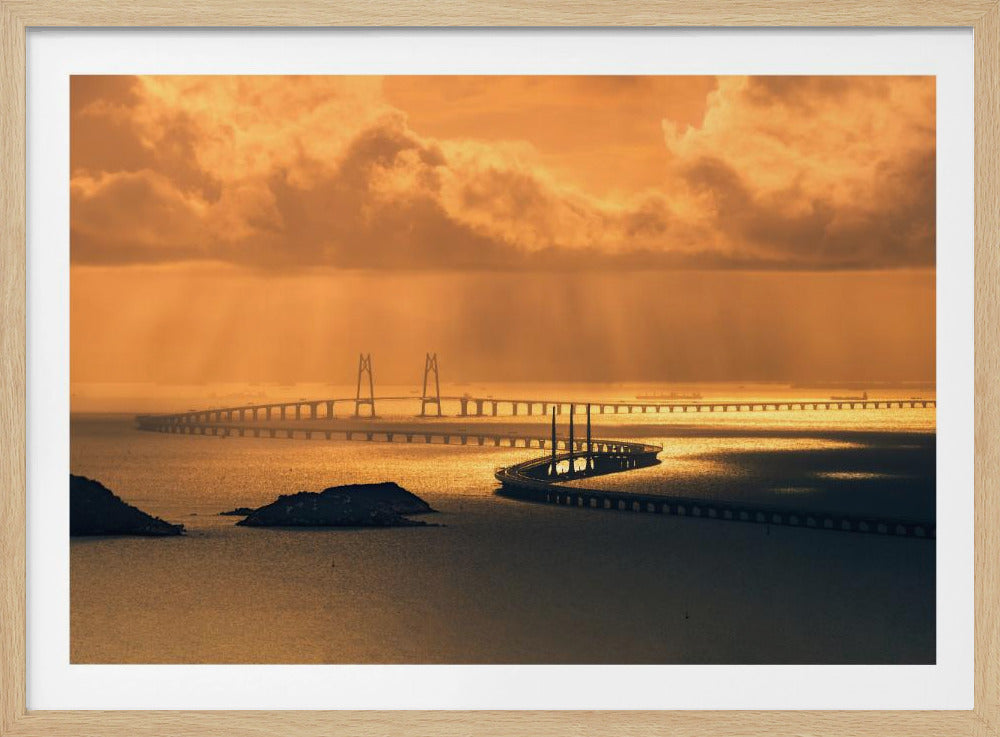A panoramic view of a massive sea-crossing bridge at sunset. The sky is filled with heavy orange clouds, and beams of golden light shine down on the reflective water, silhouetting the long, winding structure of the bridge. Wall Art