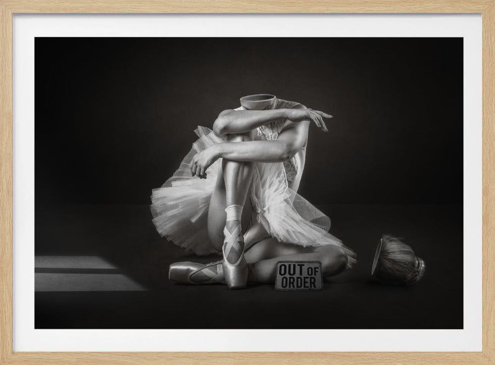 A surreal black and white photograph of a headless ballerina in a tutu sitting on the floor. Her discarded hair bun and a sign that reads 'OUT OF ORDER' are on the floor beside her. Poster