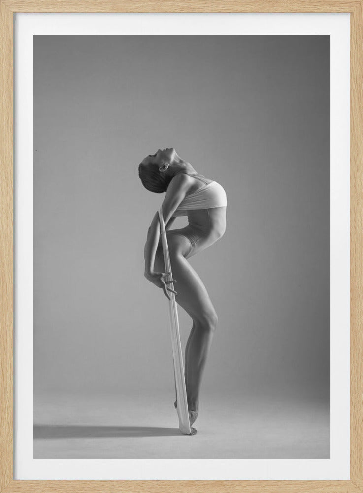A framed black and white photograph of a graceful female dancer arching her back dramatically. She holds a long white elastic band that stretches down her body to her foot, emphasizing her athletic form and flexibility against a plain studio background. Print