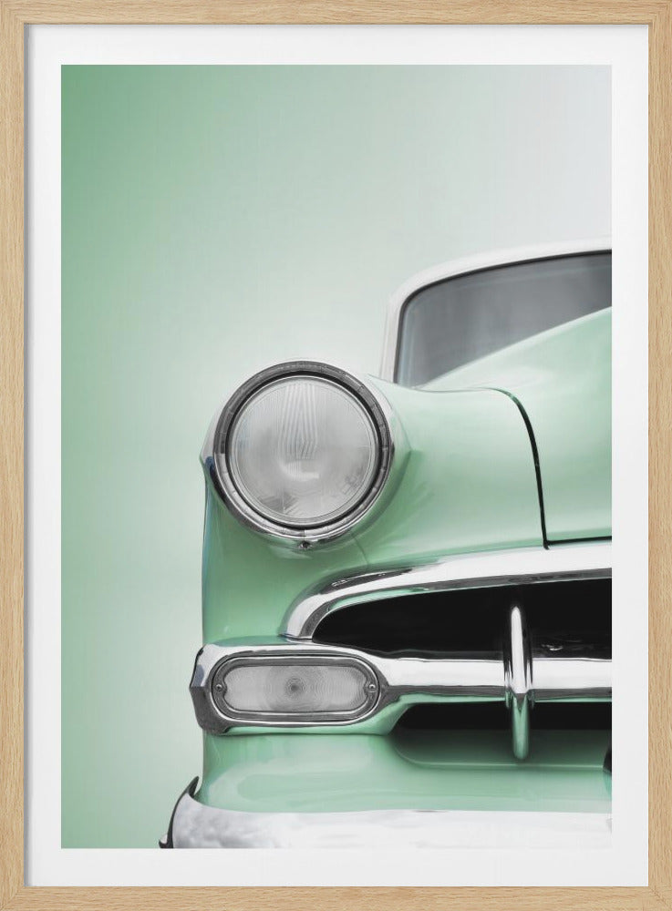 A close-up, stylized photograph of the front of a vintage car, highlighting its mint green body, large round headlight, and shiny chrome grille and bumper, all set against a matching mint green background. Poster