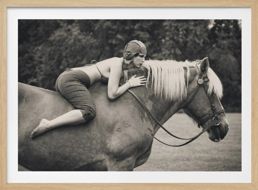 A black and white, vintage-style photograph of a woman in an aviator cap and retro clothing lying on the back of a horse. She rests her chin on her hands on the horse's white mane, looking to the side. The image is presented in a silver frame. Artwork
