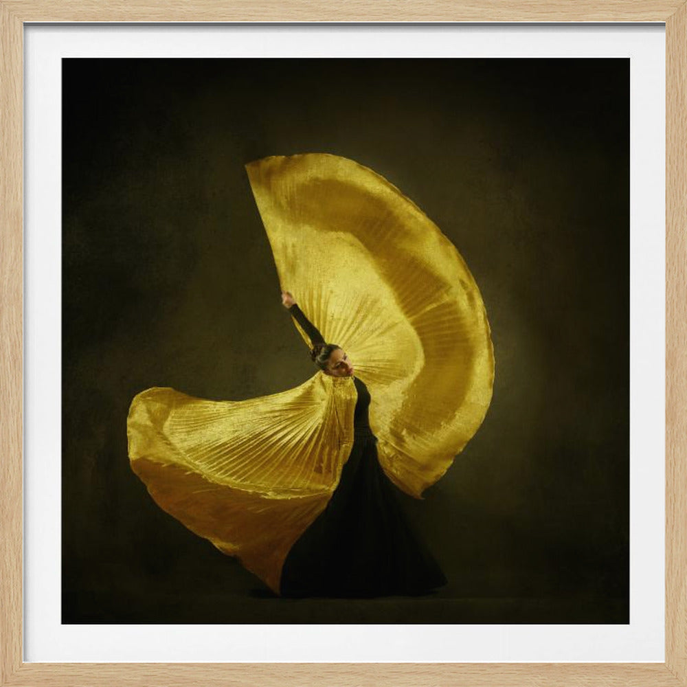 A female dancer in a black dress gracefully moves with a large, pleated, shimmering gold fabric that resembles wings, creating a dynamic swirl against a dark, moody background, all enclosed in a light wood frame. Decor