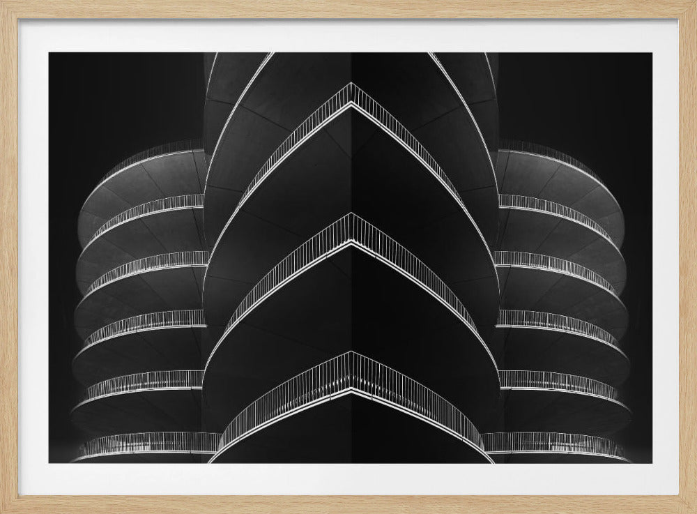 A symmetrical black and white abstract photograph of a modern building, possibly a parking garage. The composition creates a V-shape in the center with repeating levels of balconies with white railings, contrasted against a dark background, emphasizing lines and patterns. The image is presented in a silver frame. Print
