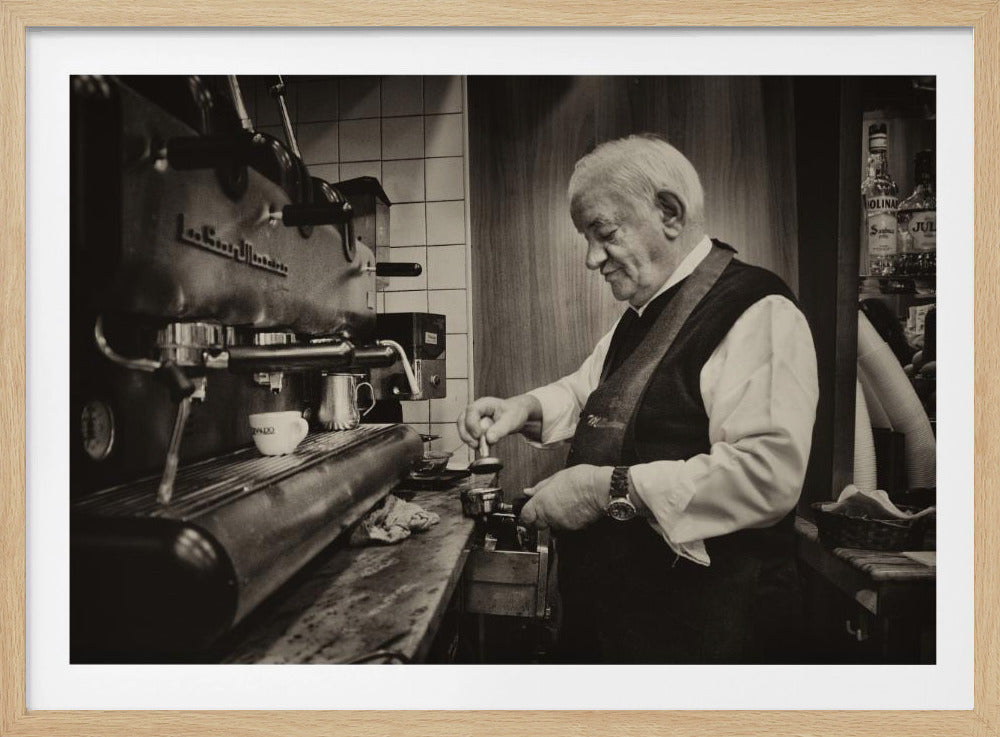 A sepia-toned, framed photograph of an elderly barista with white hair, wearing a vest, as he skillfully prepares an espresso. He is focused on his task, tamping the coffee grounds with a gentle smile, standing next to a large, vintage-style espresso machine in a cozy cafe setting. Print