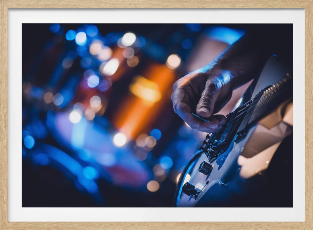 A close-up photograph of a musician's hand holding a pick and playing an electric guitar. The background is filled with blurred blue and orange stage lights, creating a bokeh effect. Poster