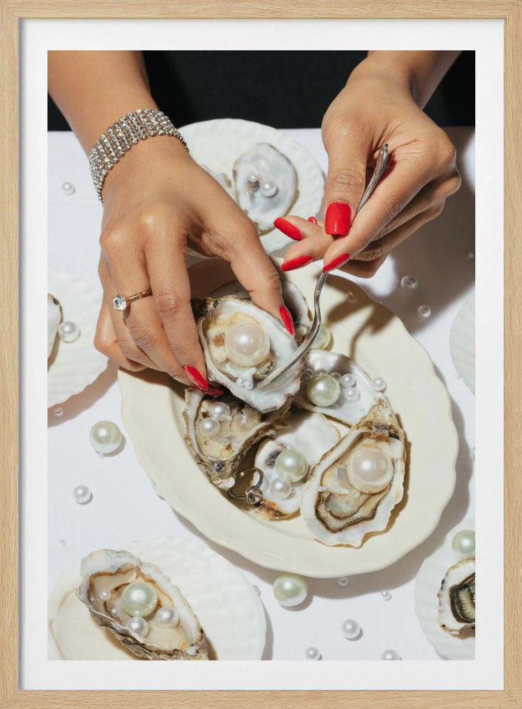 A close-up overhead shot of a woman's hands with vibrant red nails and elegant jewelry, using a fork to lift a large pearl from an oyster shell on a white plate. The plate and the surrounding white surface are adorned with numerous oysters filled with pearls of varying sizes, creating a luxurious and surreal scene. Print