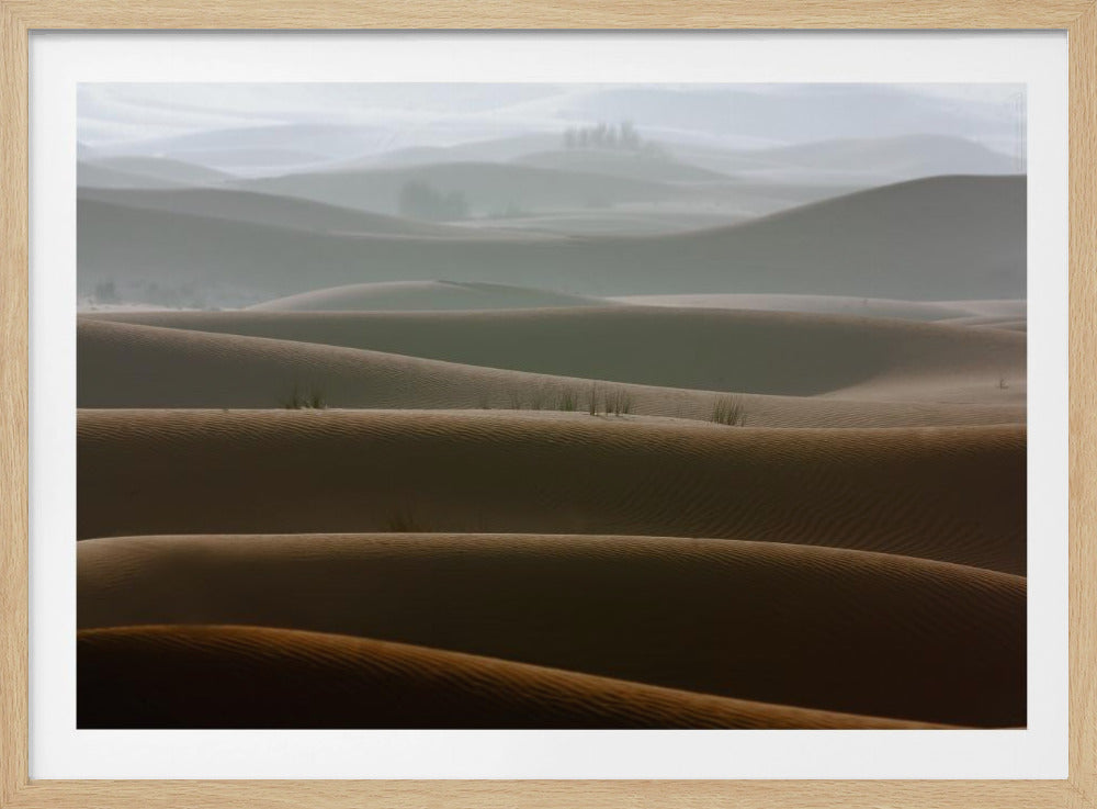 A framed photograph of a serene desert landscape, with layers of rolling sand dunes creating a sense of depth. Dark brown dunes in the foreground give way to lighter, hazy dunes and hills in the misty background. Print