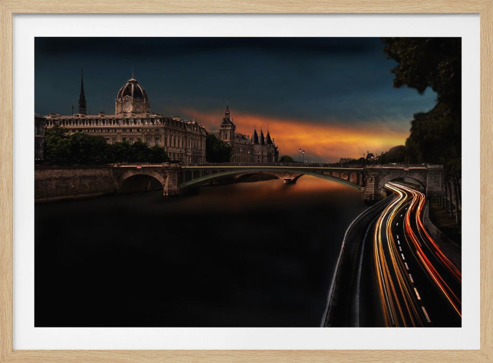 A dramatic long-exposure photograph of Paris at dusk, featuring historic buildings and a bridge over the Seine, with glowing light trails from traffic on a winding riverside road under a vibrant orange and dark blue sky. Wall Art