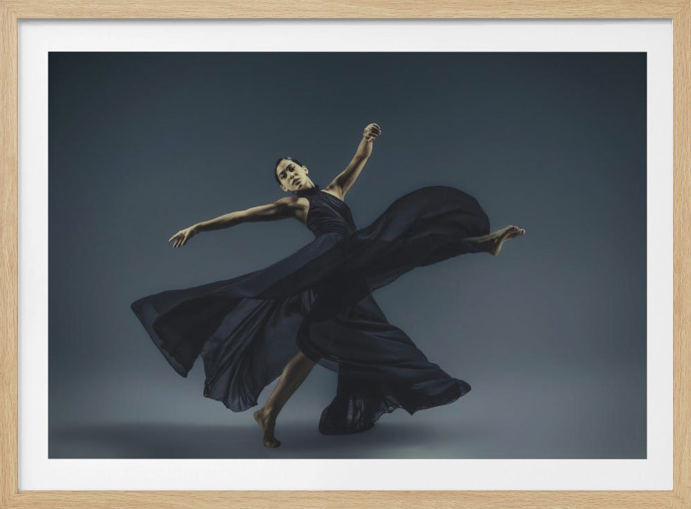 A framed photograph of a graceful female dancer in a dramatic pose, her long, dark blue, flowing dress billowing around her against a muted blue-gray studio background. Wall Art