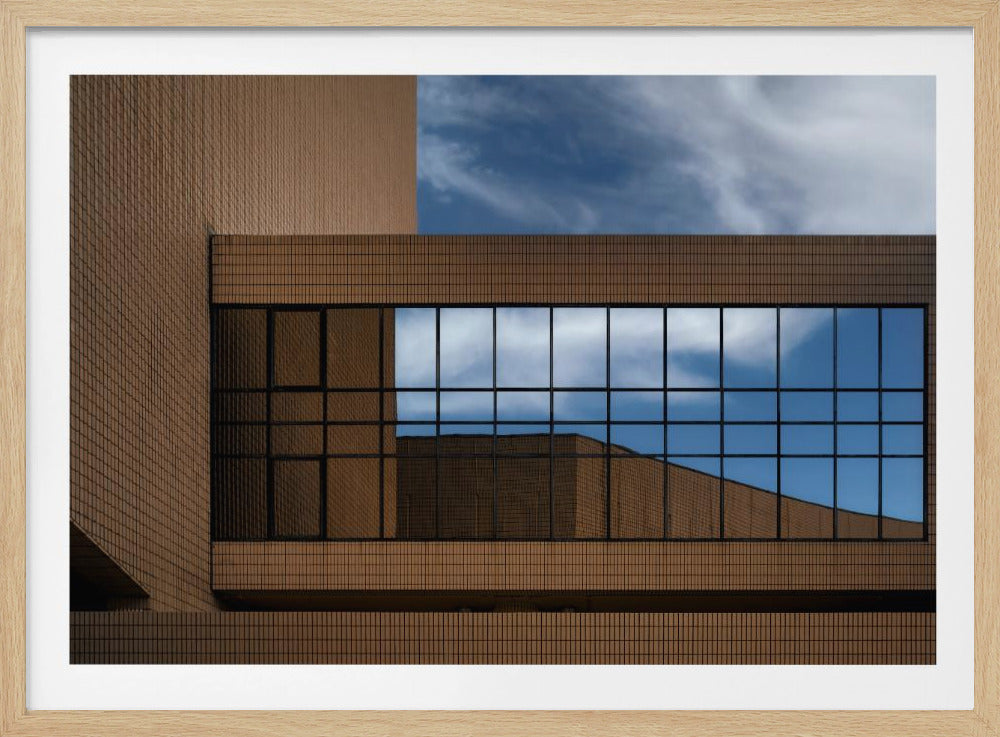 A framed architectural photo capturing the geometric lines of a brown tiled building, with a large window reflecting a brilliant blue sky and white clouds. Wall Art