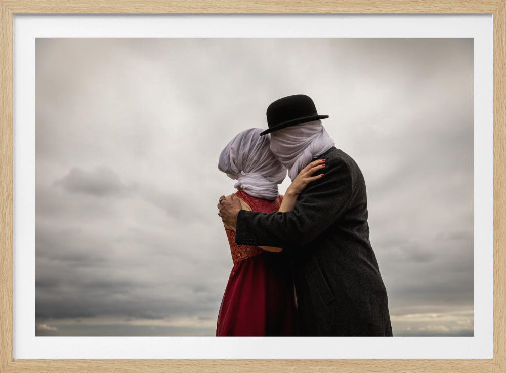 A surreal photograph shows a couple embracing passionately, their faces completely obscured by white cloths. The man wears a dark coat and a black bowler hat, while the woman is in a vibrant red dress, set against a cloudy gray sky and presented in a silver frame. Poster