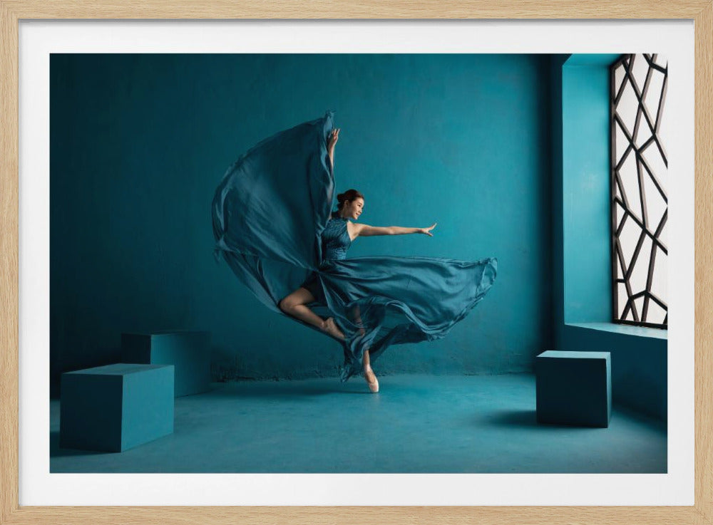 A graceful ballerina in a flowing blue dress leaps through a monochromatic blue room. Her dress billows around her as she poses elegantly on one pointe shoe, with arms outstretched. The minimalist room features blue cubes and a tall window with a black geometric design, all enclosed within a silver frame. Poster